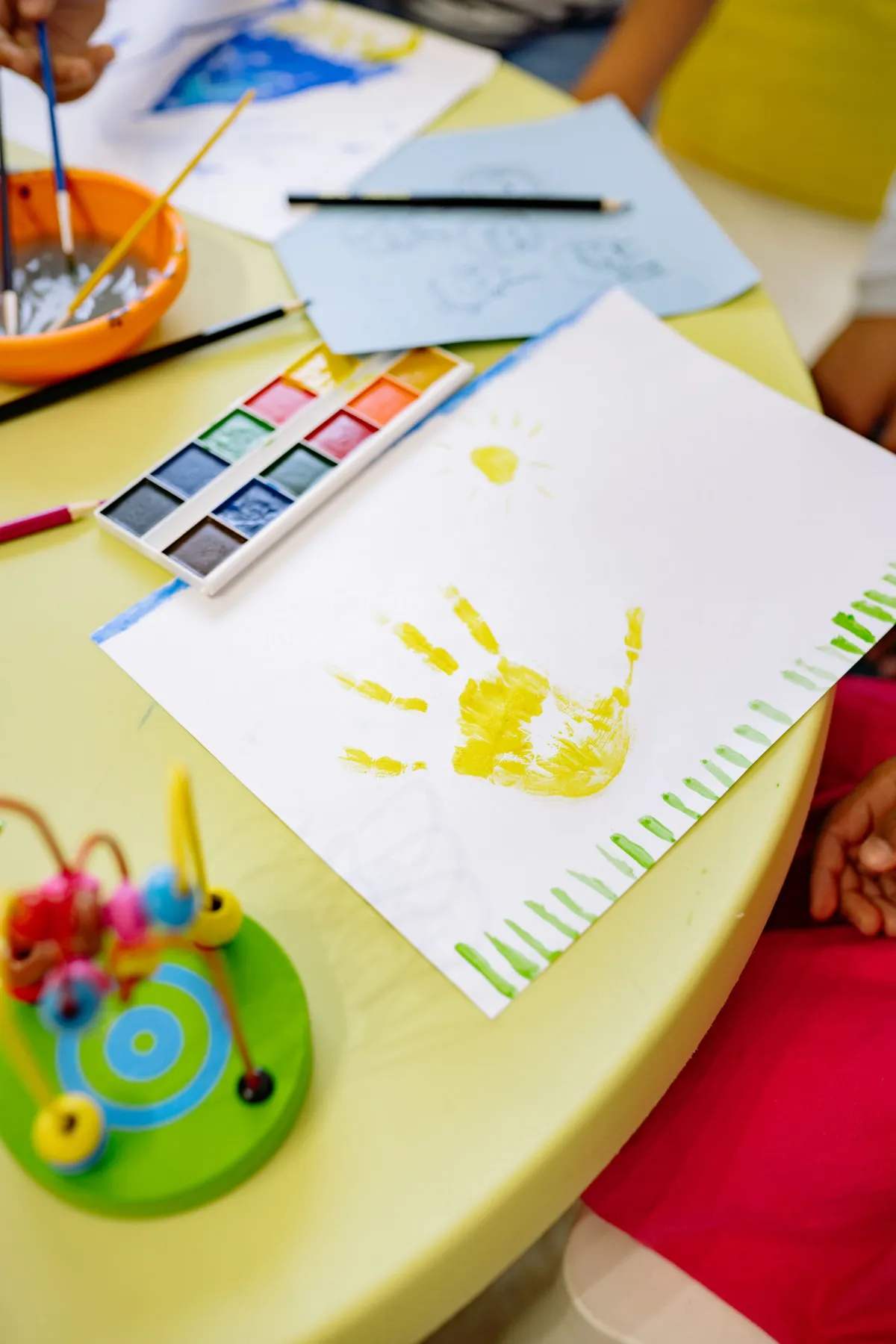 Gelber Kinderhandabdruck auf Papier neben einem Malkasten